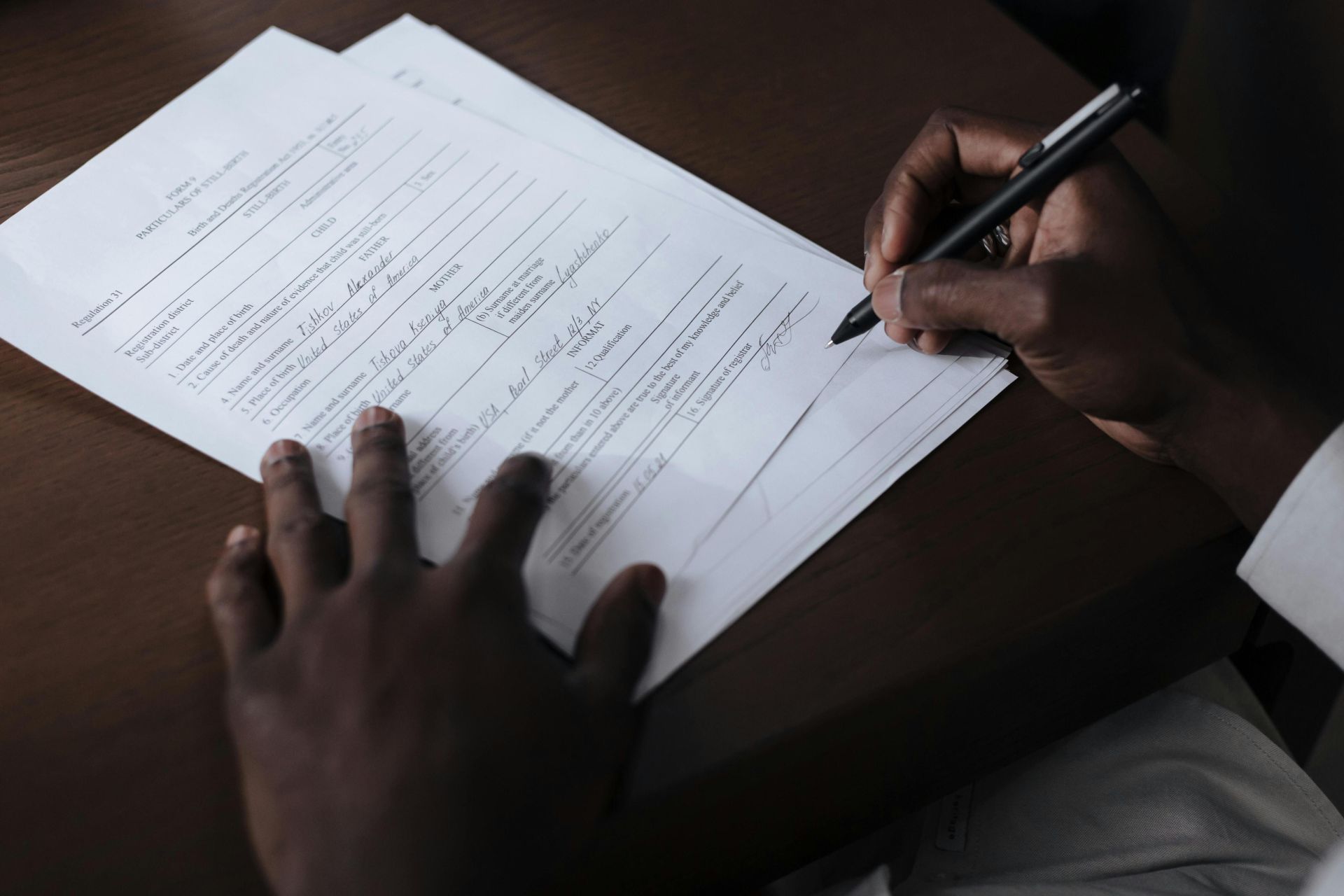 A detailed view of a man signing official documents with a pen at a table.