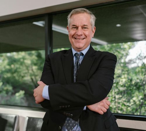 Smiling senior businessman with arms crossed standing confidently indoors.