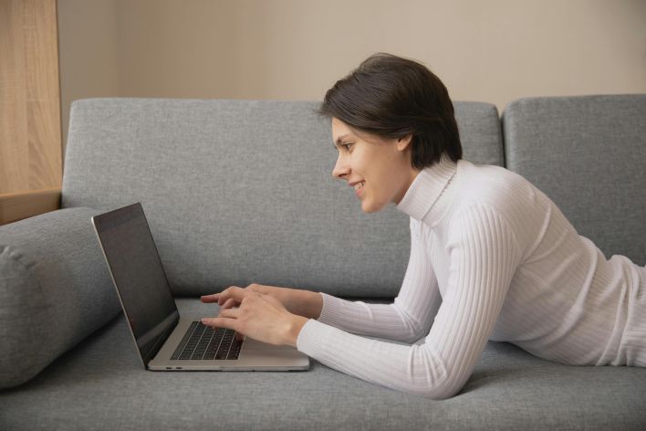 Woman working remotely on a laptop at home, lying on a comfortable sofa.
